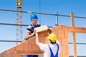 Two Bricklayer or builder or worker build or bricklaying or laying a stone or brick wall on construction or building site